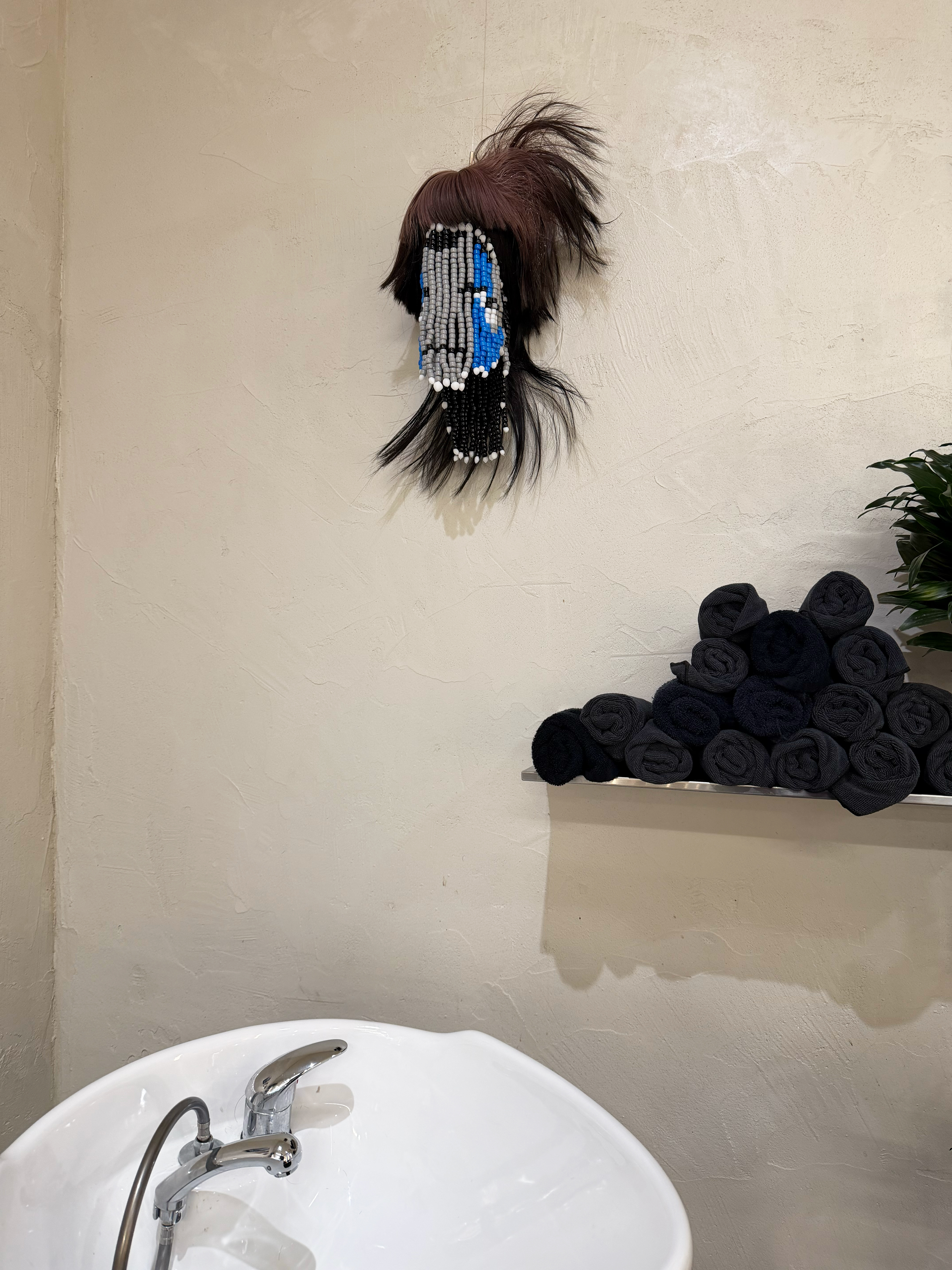 Installation shot of a sculpture made using beads and a sythetic wig to represent a floating head in a salon over a washing station.